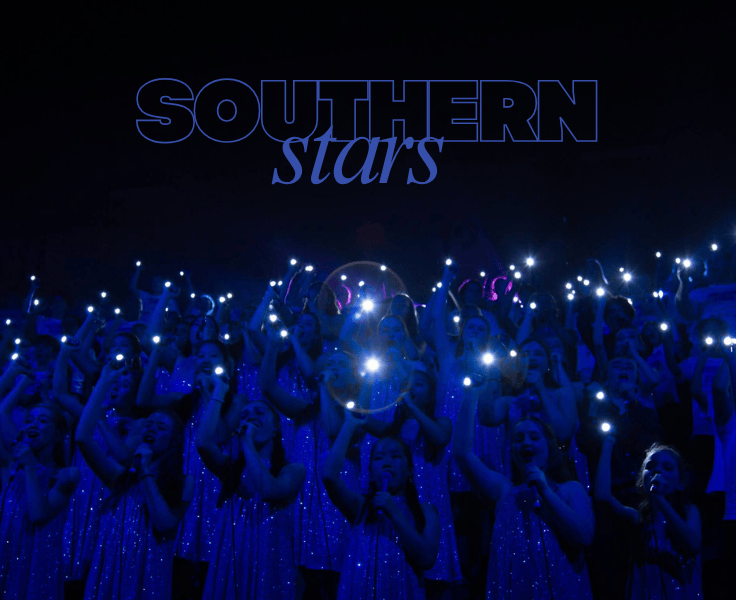 The text over the image reads 'Southern Stars' while the group of students who are in the choir all hold a microphone, the lighting is dark and tinted blue and each student has a bright light which contrasts against the dark lighting.