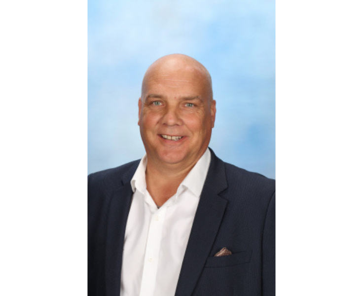 Portrait of Jason Wilkins, deputy principal of Wollongong Public School. He is smiling in front of a blue background.