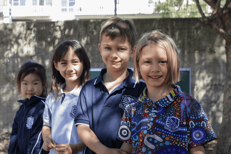 Four students, all in year 1 and 2, stand in the playground with smiles on their faces.